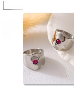 Detail of silver liquid metal rings with red zircon stones on white leather background