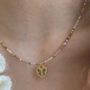 Gros plan détaillé d'un collier ras du cou perlé avec pendentif papillon doré au cou
