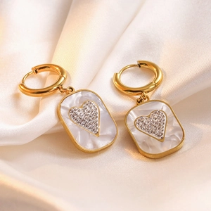 Macro view of gold rectangle earrings with white shell inlay and paved diamond heart