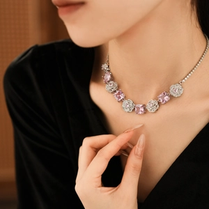 Close-up of a silver floral necklace with pink square gems on a model wearing black V-neck