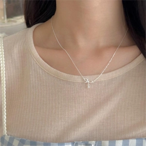 Close-up of a silver bow necklace with a zircon pendant on a model in warm lighting