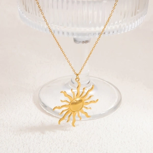 Detail shot of a 18k gold sun pendant necklace draped on textured glass surface