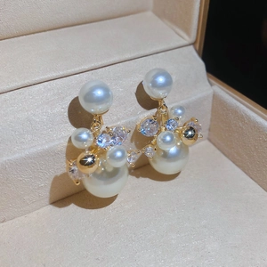Gros plan de boucles d'oreilles en perles et zircons dorées 14 carats sur velours beige