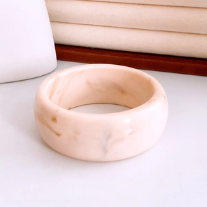 Close-up of minimalist cream resin bangle with brown marble texture on white surface