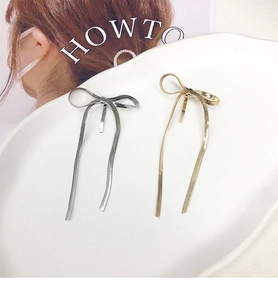Detail view of gold and silver bow hair clips with snake chain tassels on a white tray