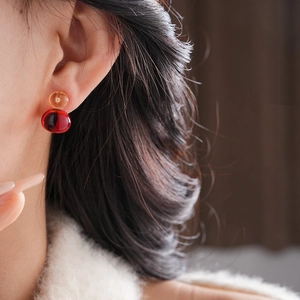 Close-up of elegant amber and burgundy resin gourd studs worn on earlobe for scale