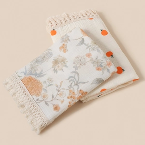 Detailed view of floral and orange print cotton swaddles with delicate beige tassels