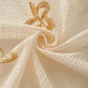Close-up of cream lace curtain with detailed golden embroidery and woven texture