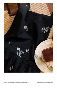 Detail of floral embroidery on black linen apron with pleated waist and cross straps