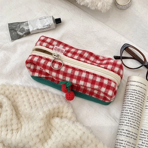 Close-up of red plaid pencil case with green base and decorative cherry charm
