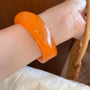 Close-up of a chunky orange acrylic resin bangle with a polished finish worn on the wrist
