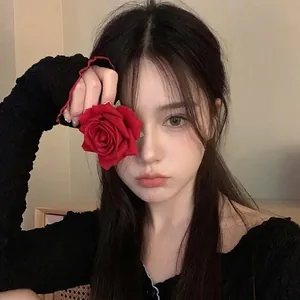 Close-up of a vintage-style red fabric rose hair clip held by a woman in soft lighting