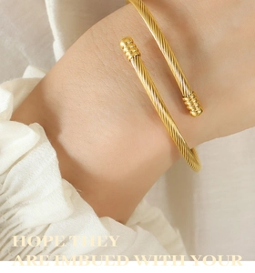 Close-up of a golden twisted rope cuff bracelet featuring cylindrical ends on a wrist