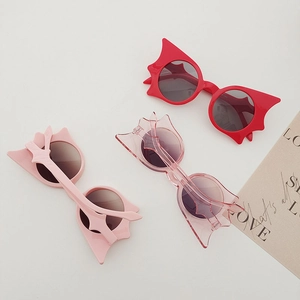 Close-up of kids' bat-shaped sunglasses in red, light pink and transparent pink colors
