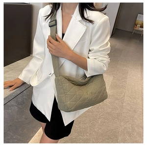 Detail of khaki quilted shoulder bag with wide strap worn by a model in a white suit