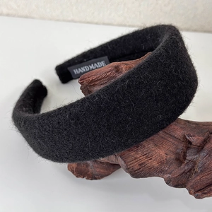 Detail of a wide black wool headband featuring a white HANDMADE label on a wooden base