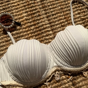 Detail view of white shell-textured bikini top with starfish charms on straw mat background