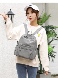 Close-up of a stylish grey nylon backpack with multiple zipper pockets on a female model
