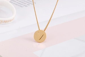 Detailed view of a gold circular titanium pendant with a minimalist engraved letter V