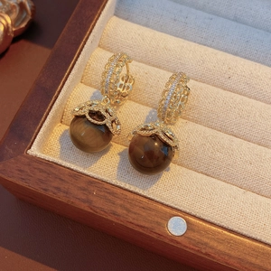 Detailed macro view of gold-plated tiger eye stone earrings with zircon lace in a box