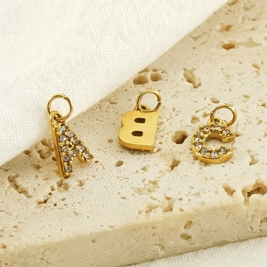 Gold stainless steel A B C letter pendants with crystals on beige stone surface