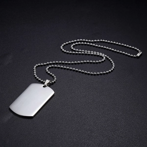 Macro shot of silver rectangle dog tag pendant with classic bead chain on dark surface