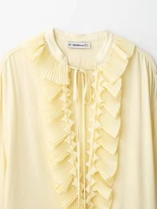 Close-up of a light yellow V-neck blouse with ruffled edges and tie collar detail