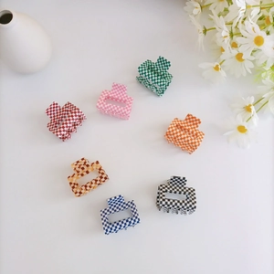 Flat lay of small checkered acrylic hair claws in multiple colors with daisy decor