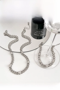 Detailed view of silver heart rhinestone necklace and Cuban chain on a reflective glass surface