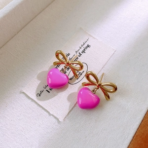 Détail macro de boucles d'oreilles cœur rose et nœud doré dans un coffret de luxe