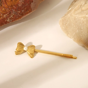 Dettaglio di un fermaglio dorato a fiocco con perla su un elegante sfondo di pietra