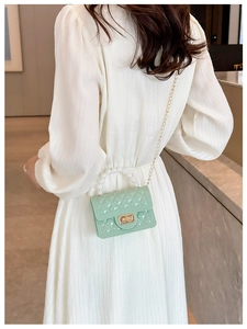 Model wearing a small green jelly handbag with pearl handle and gold chain strap