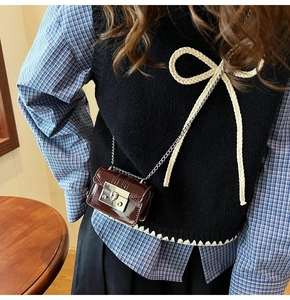 Close-up of a deep brown patent leather mini bag with metal chain on a model