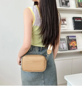 Detail of khaki pebbled leather camera bag featuring a wide colorful woven strap