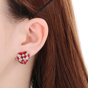 Close-up of a red heart-shaped checkerboard earring with diamonds on a model's ear