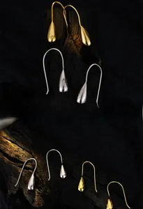 Macro detail of glossy silver and gold teardrop earrings on black textured background