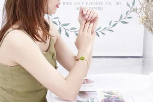 Detail view of a gold chain bracelet featuring a green gemstone and small heart pendant