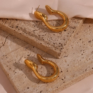 Detail of minimalist U-shaped gold earrings placed on marble and silk fabric