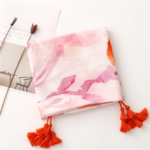 Detail of colorful watercolor print scarf with bright orange tassels on a white background