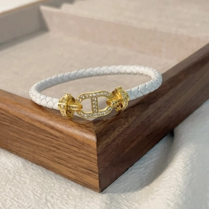 Dettaglio del bracciale in pelle intrecciata bianca con chiusura dorata e micro-pavé