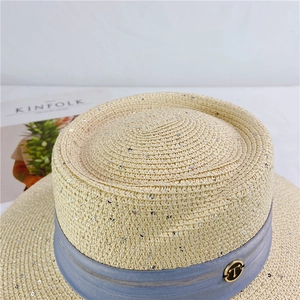 Detailed macro view of woven straw hat featuring shimmering sequins and blue ribbon band