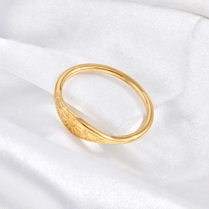 Macro detail of gold stainless steel ring with sun pattern texture on white satin