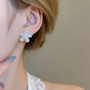Elegant flower stud earrings with shimmering zircons and pearls worn on model ear