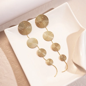 Detail of gold drop earrings with textured circular metal discs in graduated sizes