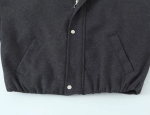 Macro detail of elastic hem, metal zipper, and snap pocket on charcoal gray wool jacket