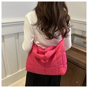 Rear view of model wearing a fuchsia quilted puffer shoulder bag with wide strap