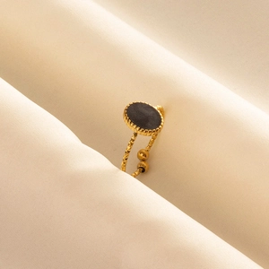 Adjustable gold plated stainless steel ring with black enamel oval inlay on beige fabric