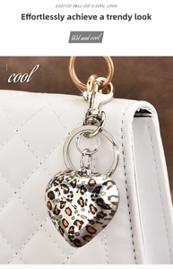 Detail of leopard print heart keychain with silver lobster clasp on a white leather bag