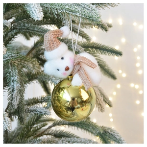 Close-up of plush bear ornament with gold bauble hanging on a snowy Christmas tree