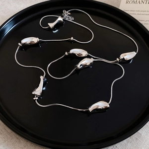 Macro shot of silver liquid metal pendants on a sleek snake chain over a black tray